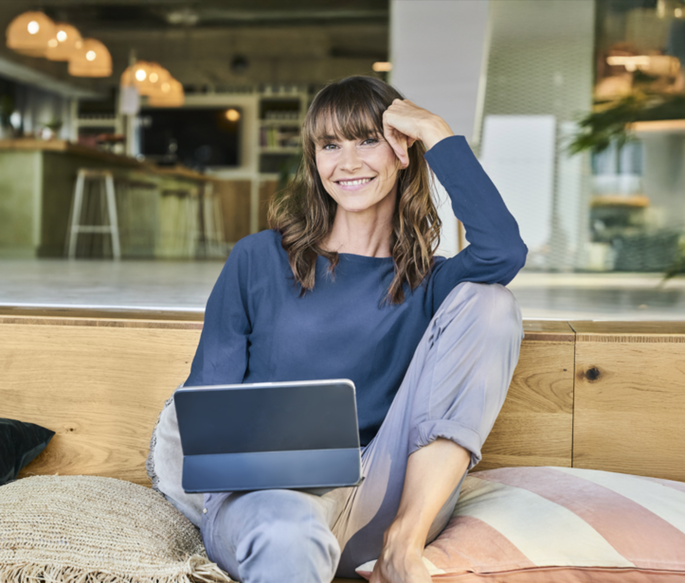 Frau sitzt lächelnd auf einem Sofa und hält ein Laptop auf dem Schoss.